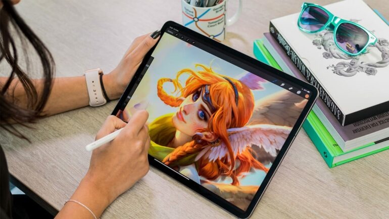 Close-up of a digital artist sketching a character portrait on an iPad at a desk with books and sunglasses.