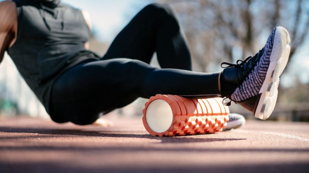 Close-up of a person rolling out their leg muscles on an orange foam roller after a soccer match.