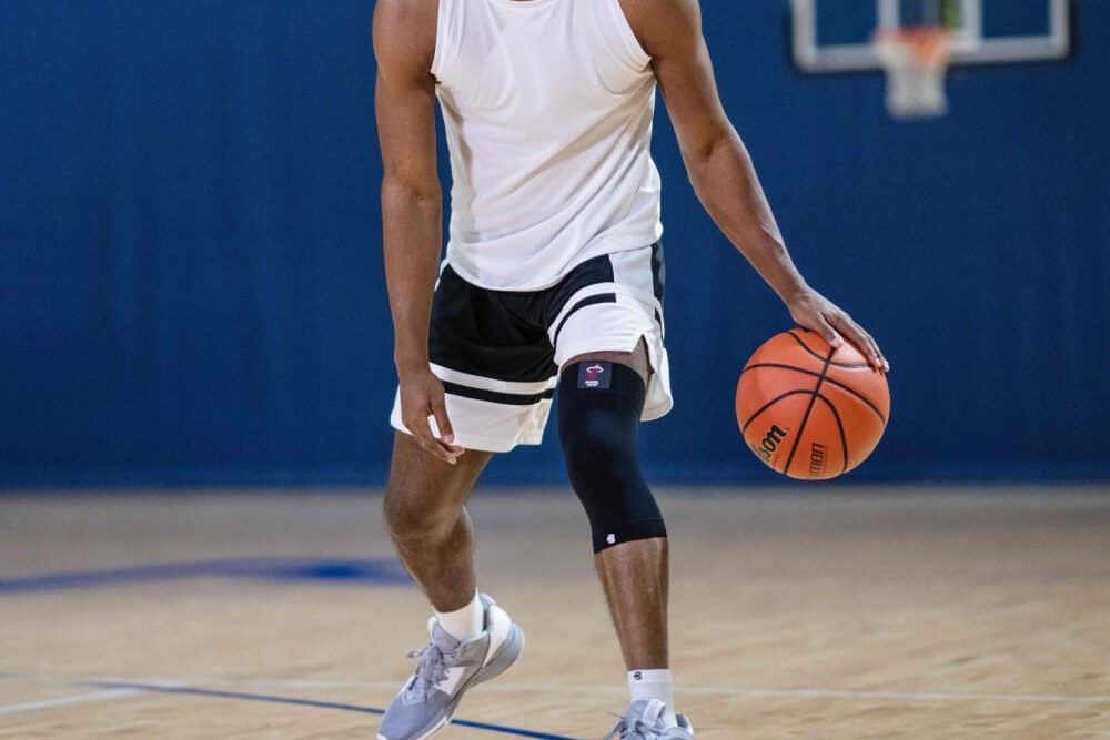 Basketball player wearing a black compression knee sleeve while dribbling on court.