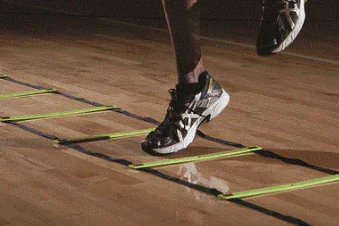 Athlete's feet moving through a yellow agility ladder on a gym floor for basketball speed training.